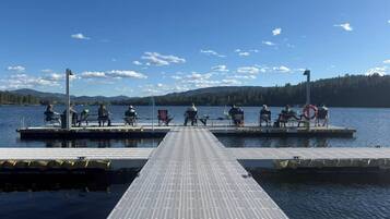 Un muelle con gente sentada, un flotador salvavidas y un lago tranquilo con montañas al fondo.