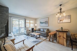 Ein modernes Wohnzimmer mit Kamin, einer Couch, einem Couchtisch und einem Essbereich mit Holztisch und Bänken.