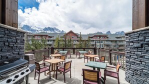 Un patio con mobiliario exterior y una parrilla, con vistas a una cadena montañosa.