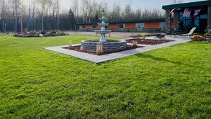 A well-maintained lawn with a central fountain, a building with a green roof, and a flag.