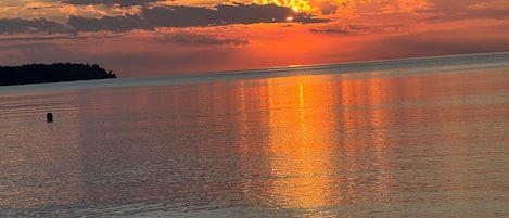 A sunset over a calm body of water with a silhouette of land in the distance.