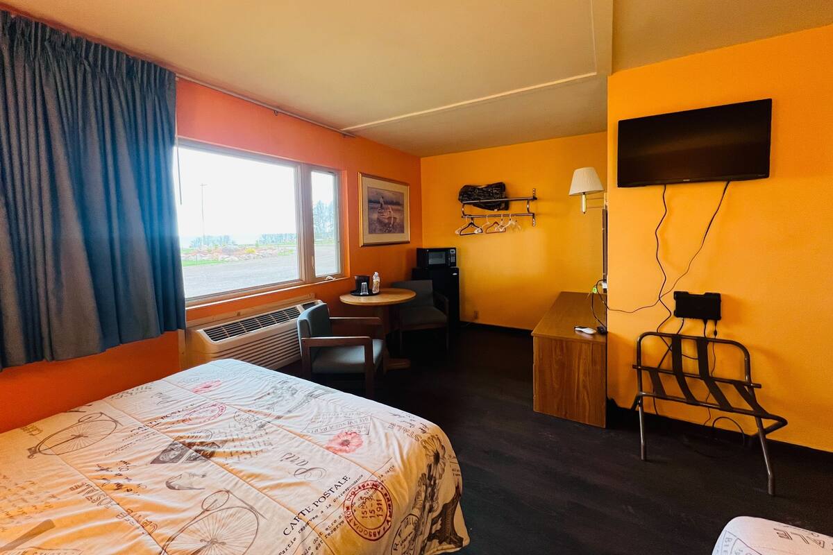 A hotel room with a bed, a desk, a chair, a television, and a window with curtains.