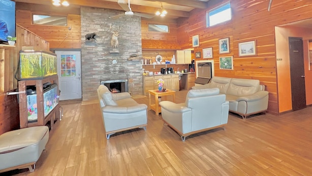 A spacious living area with a fireplace, wooden walls, and a kitchen in the background.
