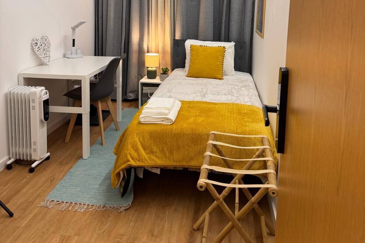 A compact hotel room with a bed, bedside table, lamp, and a small desk with a chair.