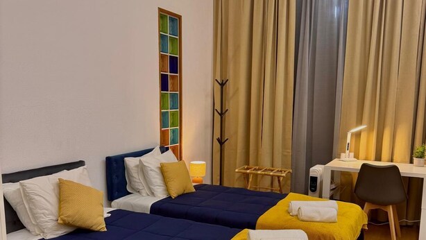 Habitación de hotel con dos camas, un escritorio, una silla, una lámpara y un perchero.