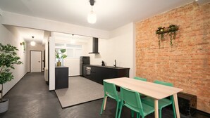 Una cocina moderna con pared de ladrillo, un comedor con mesa y sillas, y un pasillo que conduce a una puerta.