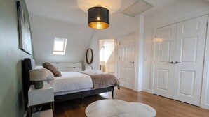 A bedroom with a bed, bedside table, lamp, round table, and a hanging light fixture. - Stylish Home | Families | Groups | Contractors (Cheshire West and Chester)