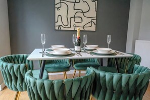 A dining table set with plates, cutlery, and glasses, surrounded by green upholstered chairs. - Stylish Home | Families | Groups | Contractors (Cheshire West and Chester)