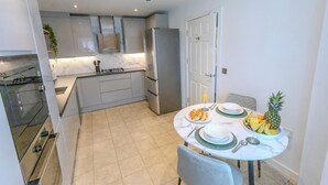 A compact kitchen with modern appliances, a dining table set with plates and cutlery, and a fruit bowl. - Stylish Home | Families | Groups | Contractors (Cheshire West and Chester)
