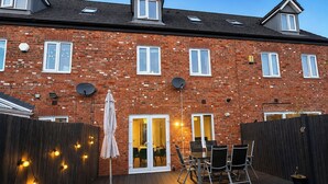 A brick house with a patio, outdoor seating, and a door leading to an interior space. - Stylish Home | Families | Groups | Contractors (Cheshire West and Chester)