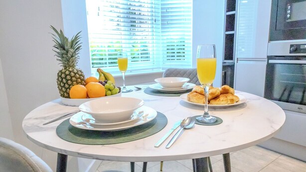A breakfast setting with a table, fruit bowl, croissants, and orange juice. - Stylish Home | Families | Groups | Contractors (Cheshire West and Chester)