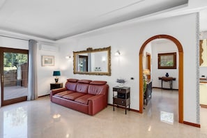Un salón amplio con un sofá de cuero, un espejo y un área de comedor visible a través de un arco.