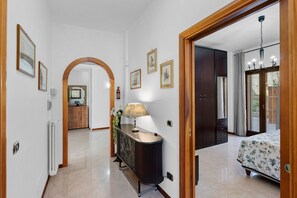 Un pasillo con una puerta de madera, una consola con una lámpara, cuadros enmarcados y un radiador.