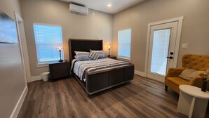 Ein Schlafzimmer mit einem Bett, Nachttischen, einer Lampe, einem Sessel und einer Tür.