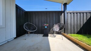 Eine Terrasse mit zwei schwarzen Stuhlgestellen aus Draht, einem kleinen Tisch mit einem Blumentopf und einem Holzzaun.