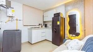 Ein kompaktes Hotelzimmer mit einer Küchenzeile, einem Bett mit gemustertem Überwurf und einem an der Wand befestigten Spiegel.