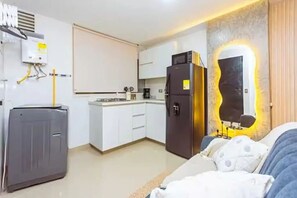 Ein kompaktes Hotelzimmer mit einer Küchenzeile, einem Bett mit gemustertem Überwurf und einem an der Wand befestigten Spiegel.