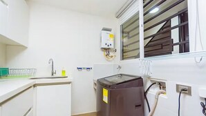 Eine kleine Küche mit Spüle, einem Kühlschrank, einer Waschmaschine und einem Fenster mit Jalousien.