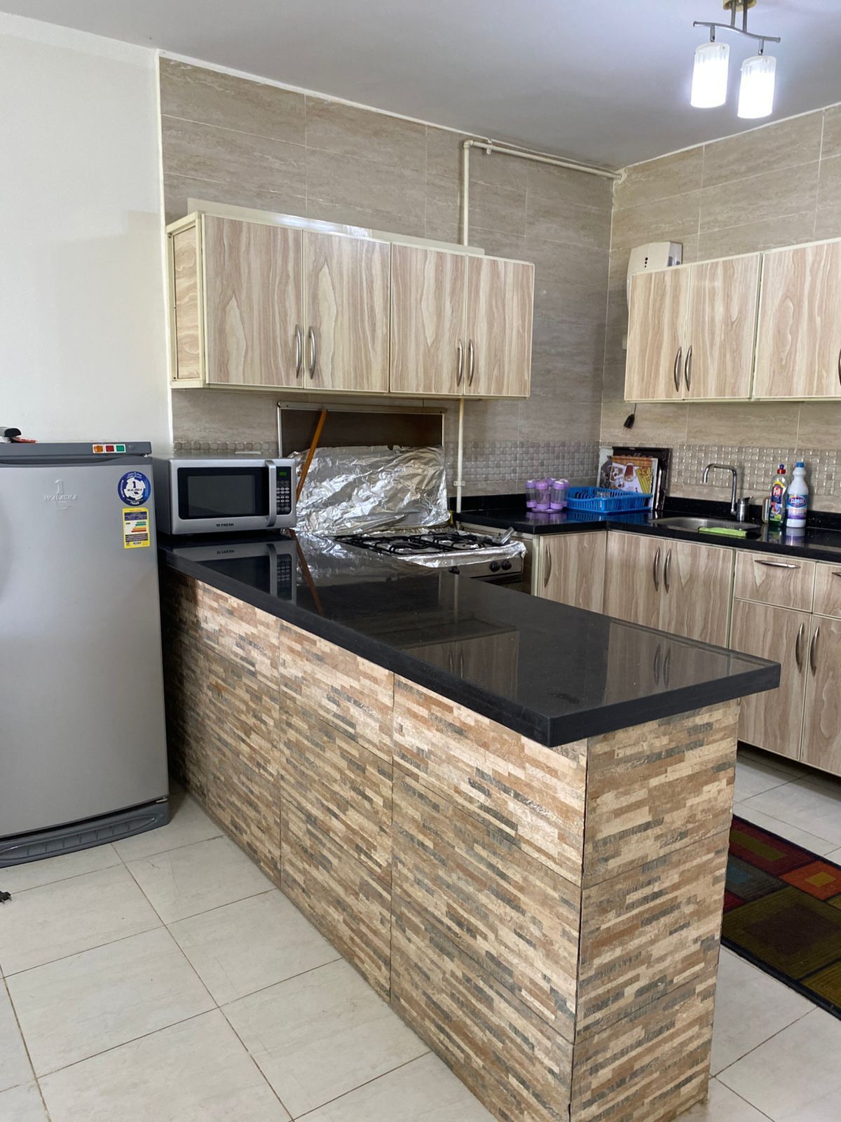 A kitchen with a central island, wooden cabinets, a refrigerator, a microwave, and a gas stove.