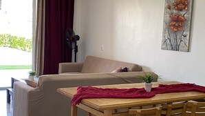Ein Wohnzimmer mit einer Couch, einem Esstisch mit Stühlen, einer Zimmerpflanze und einer Klimaanlage an der Wand.