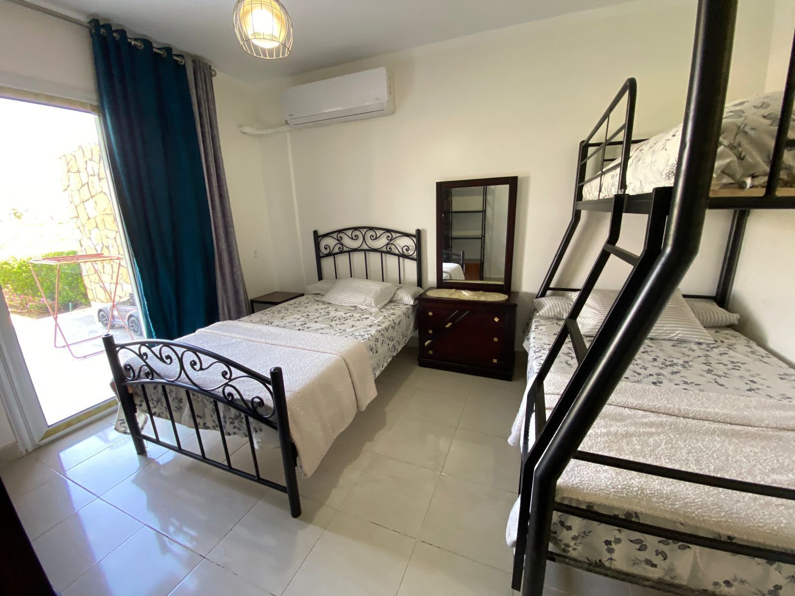 Una habitación con cama, cómoda, espejo y ventana con cortinas.