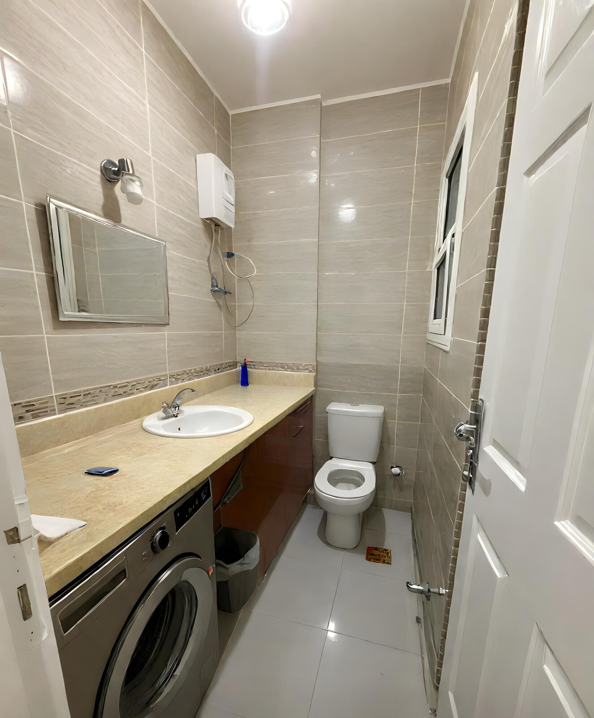 A compact bathroom with a washing machine, two sinks, a toilet, and a mirror.