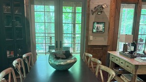 A dining area with a long table, chairs, a unique bowl centerpiece, wooden cabinets, and large windows.