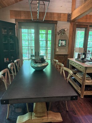 Un espace repas avec une longue table, des chaises, un centre de table original en forme de bol, des meubles en bois et de grandes fenêtres.