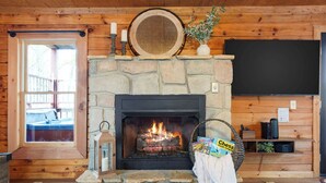 A stone fireplace with a fire, a television on the wall, and a window with a view of a deck. - Location, Smoky Mountain View, Hot Tub, Games! (Sevierville)