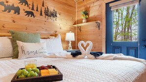 Een gezellig slaapkamer in een houten hutje met een bed, kussens, een schaal fruit en een muurschildering.