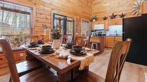 A wooden interior with a dining table set for four, a kitchen area, and a large window with blinds. - Location, Smoky Mountain View, Hot Tub, Games! (Sevierville)