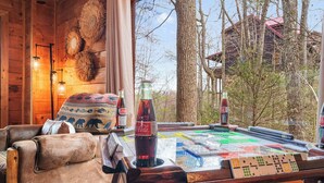 A wooden cabin interior with a large table, leather chairs, and a view of trees and buildings outside. - Location, Smoky Mountain View, Hot Tub, Games! (Sevierville)