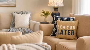 Ein Wohnzimmer mit einem beigefarbenen Sofa, gemusterten Kissen, einer Lampe und einem gerahmten Bild an der Wand.