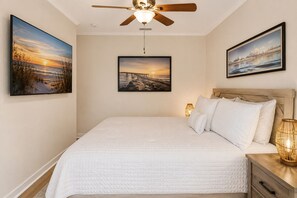 Ein Schlafzimmer mit einem Bett, einem Deckenventilator, einem Nachttisch mit Lampe und drei gerahmten Bildern an der Wand.