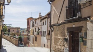 Uma rua de paralelepípedos estreita, ladeada por edifícios tradicionais, uma parede de pedra e um carro estacionado.