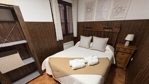 Un dormitori amb un panell de fusta al capçal, un llit amb roba de llit blanca, una tauleta de nit amb una làmpada i un armari de fusta.