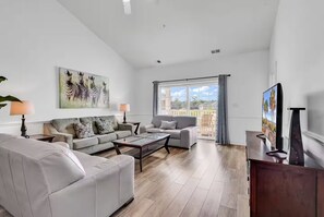 Ein geräumiges Wohnzimmer mit einer Couch, Sesseln, einem Couchtisch und einem Fernseher.
