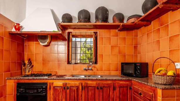 A kitchen with a gas stove, sink, microwave, and wooden cabinets. - Can Pere - 3-bedroom Villa for 7 Guests (Sant Joan de Labritja)