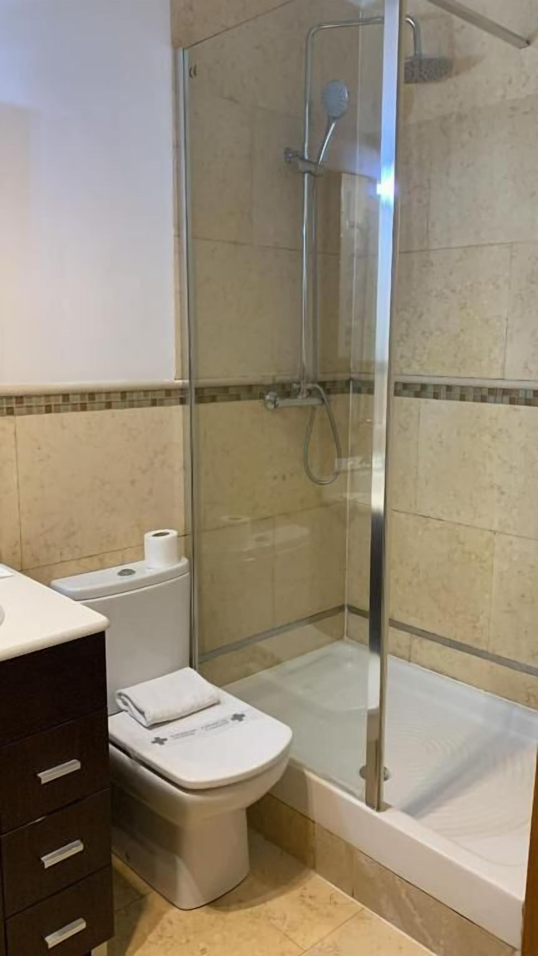 Un baño con ducha envuelta en vidrio, inodoro y lavamanos con mueble oscuro.