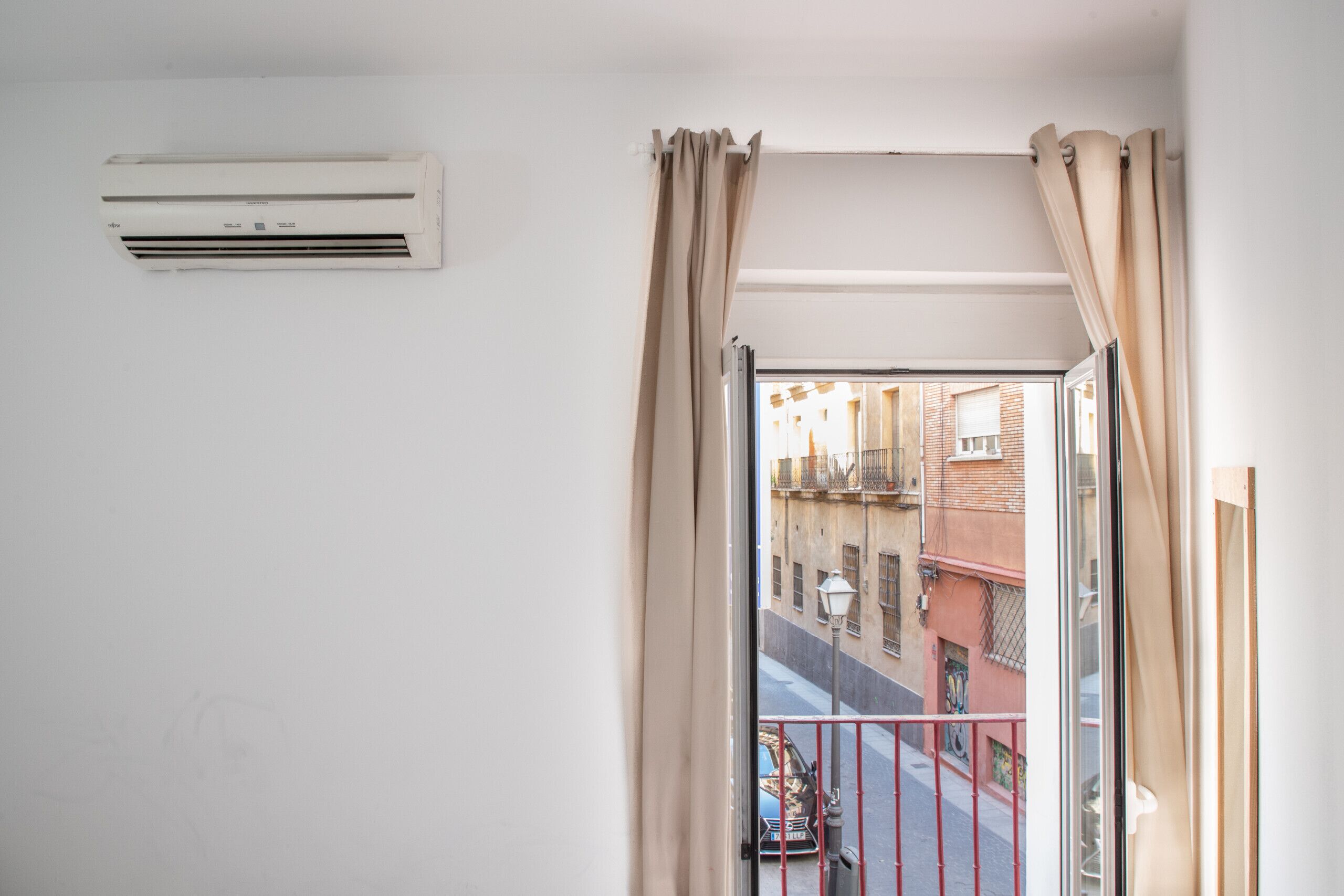 A room with a window, beige curtains, and an air conditioning unit on the wall.