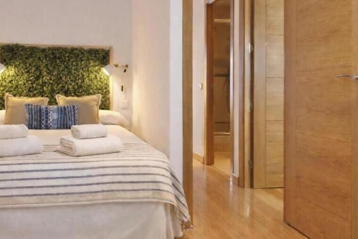 Habitación de hotel con cama, almohadas, cabecera con plantas y una puerta de madera.