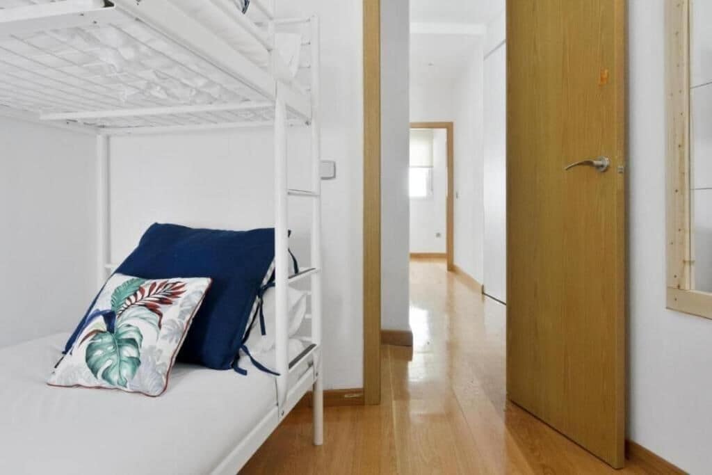 Een stapelbed met een kussen en een sierkussen, een houten deur en een gang naar een andere kamer.