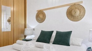 A hotel room with a bed, two pillows, a nightstand with a lamp, and two woven hats on the wall. - Collection Gran Vía (Madrid)