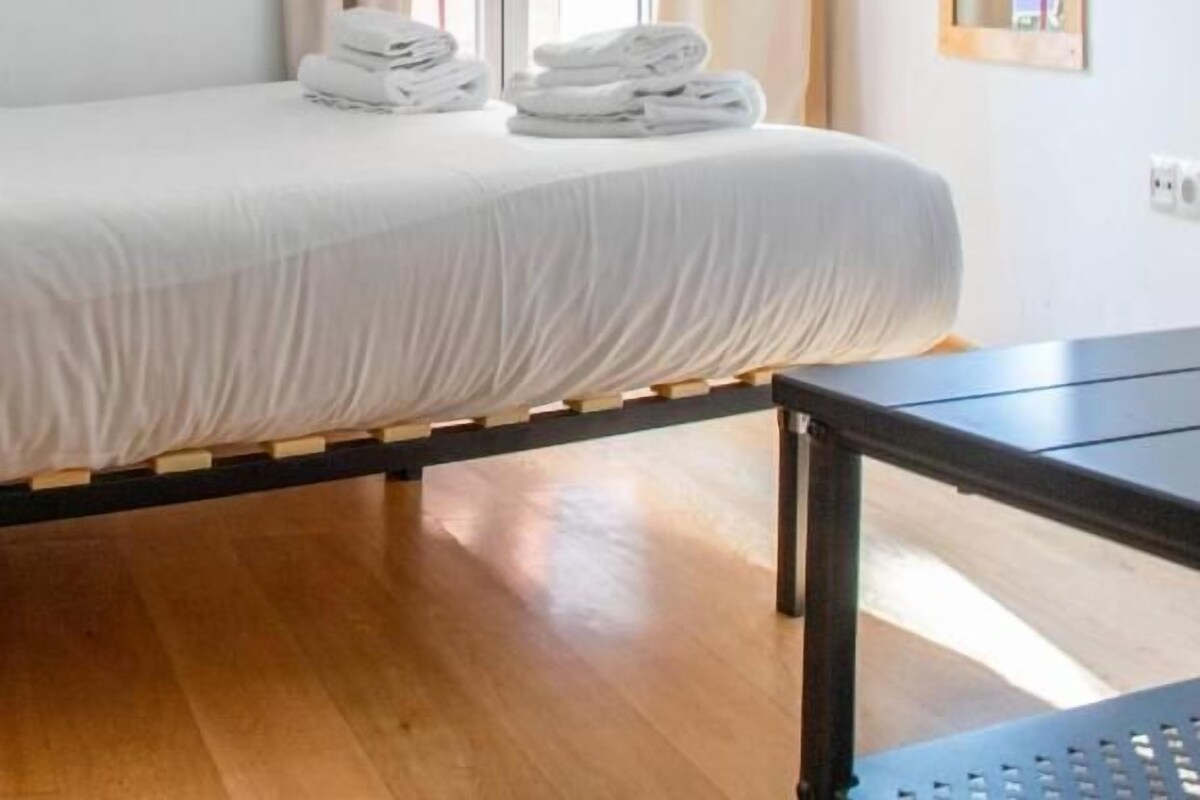 Una habitación con cama, una mesa y un ventanal con cortinas.