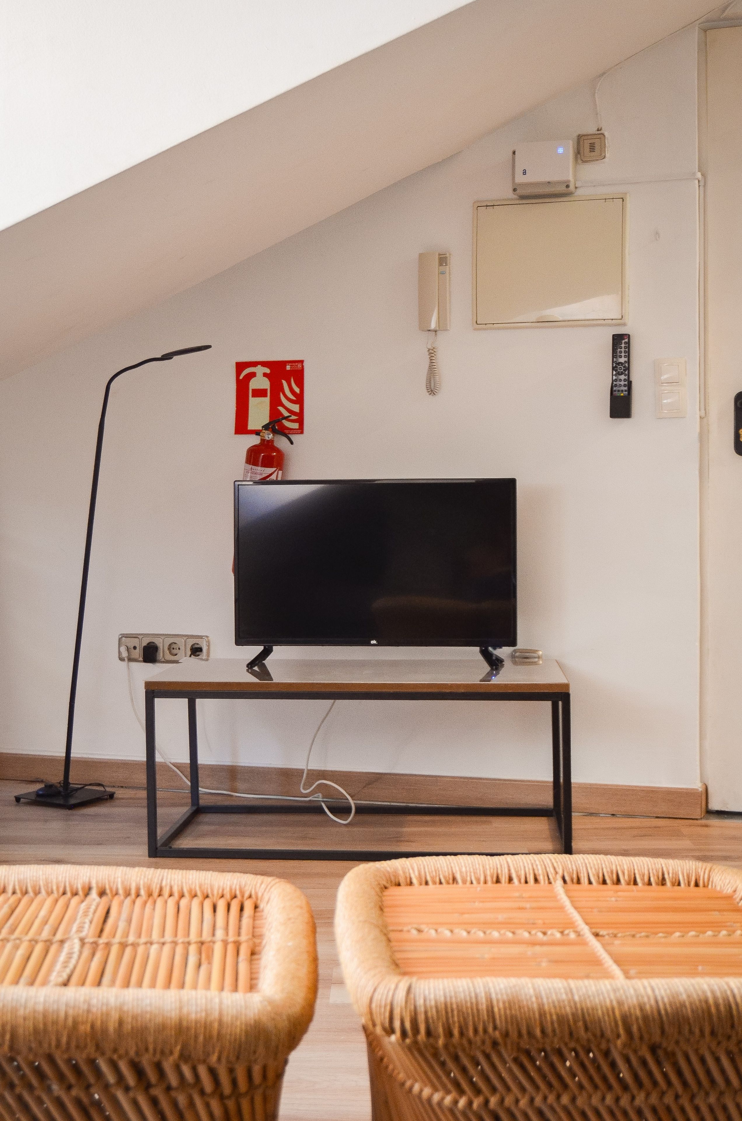 Une pièce équipée d’un téléviseur posé sur un meuble, d’un extincteur, d’une télécommande et d’une prise électrique au mur.