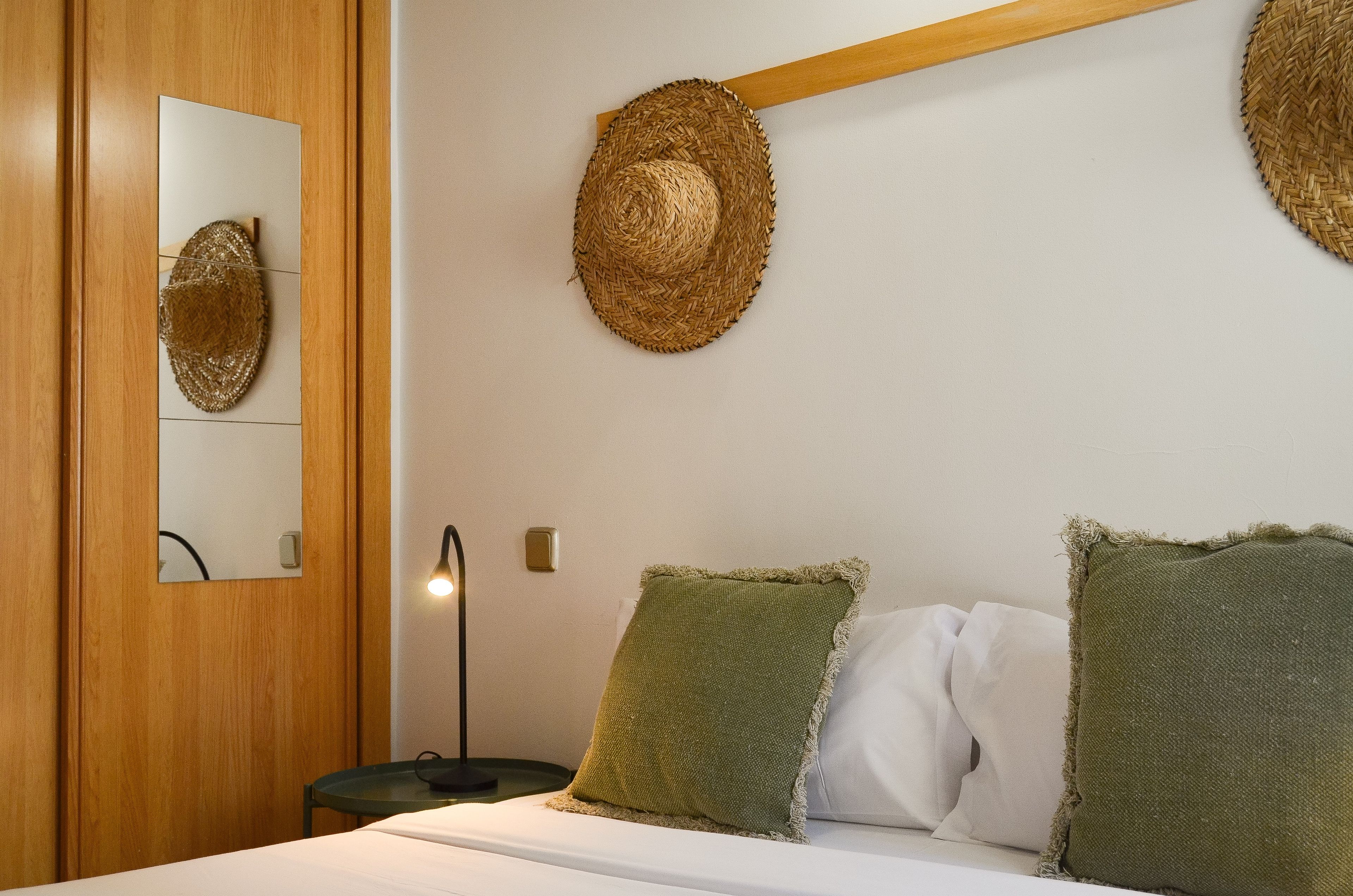 Ein Schlafzimmer mit Bett, Kissen, einem Nachttisch, einer Lampe und einem Wandspiegel.