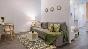 A modern living room with a grey sofa, a small side table, a dining area with a table and chairs, and a kitchen area in the background. - Collection Gran Vía (Madrid)