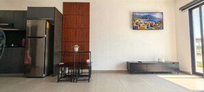 Eine moderne Küche mit Kühlschrank, einer Wandpaneele aus Holz, einem Esstisch mit Stühlen und einem Gemälde einer Küstenstadt.