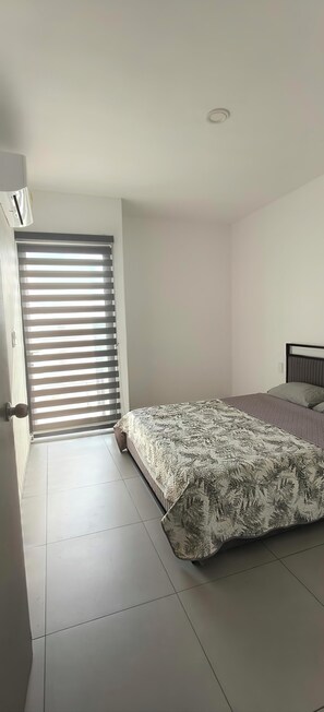 Ein Schlafzimmer mit einem Bett, einem Fenster mit Jalousien und einer Tür.