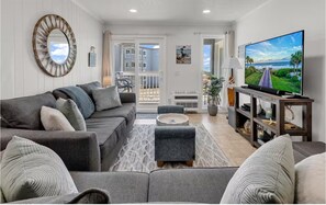 A living room with a grey sofa, a coffee table, a TV on a wooden stand, and a view of the outside balcony. - Oceanfront Escape Shore Dr Condo Balcony (Myrtle Beach)